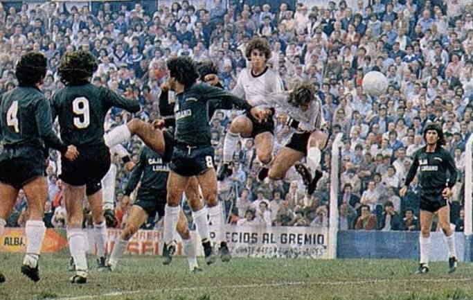Hinchas viendo un clásico en un bar deportivo con tensión en el ambiente